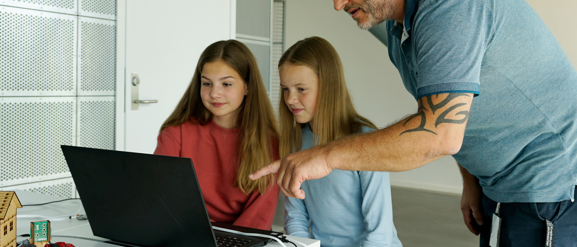 Lærer viser hvordan to jenter skal programmere microbit